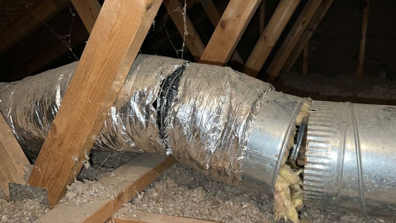Flex duct joint in an attic wrapped with mismatched tape, showing an inconsistent seal at the connection